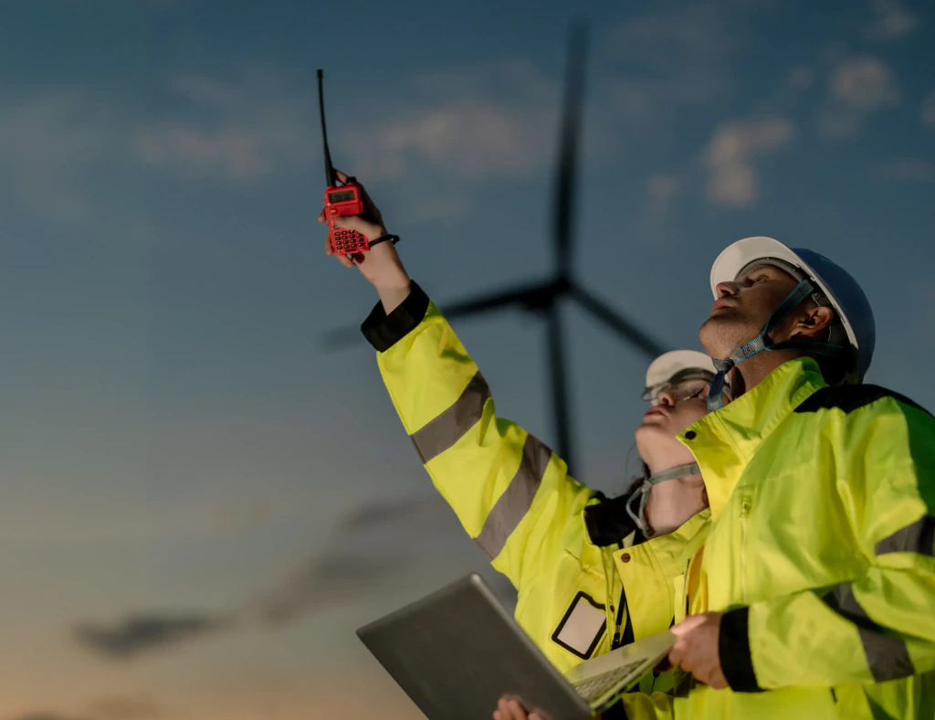 Owner's team engineers in hi-vis gear directing work at a wind farm at dusk